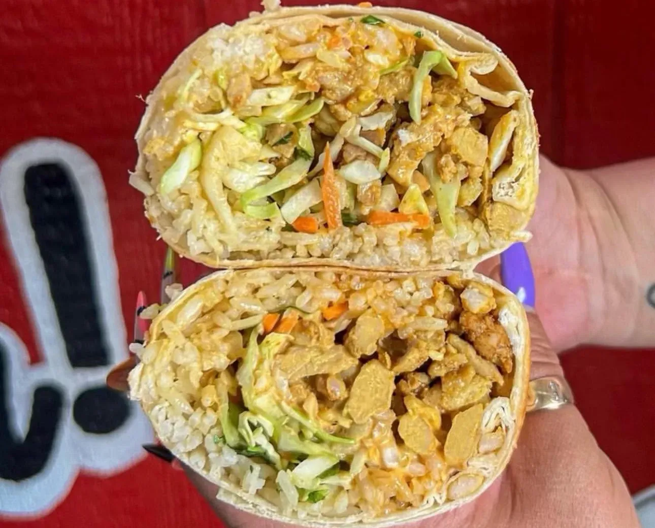 El Fat Cat Grill burrito cut in half, held up against the red storefront wall
